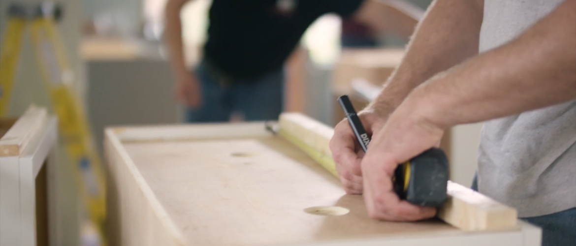Kitchen contractor measuring a strip of wood with a tape measure and marking the wood