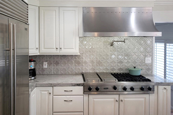 Stainless steel cooktop with matching range hood, wall faucet, grey tile backsplash and white cabinets Stainless steel cooktop with matching range hood, wall faucet, grey tile backsplash and white cabinets