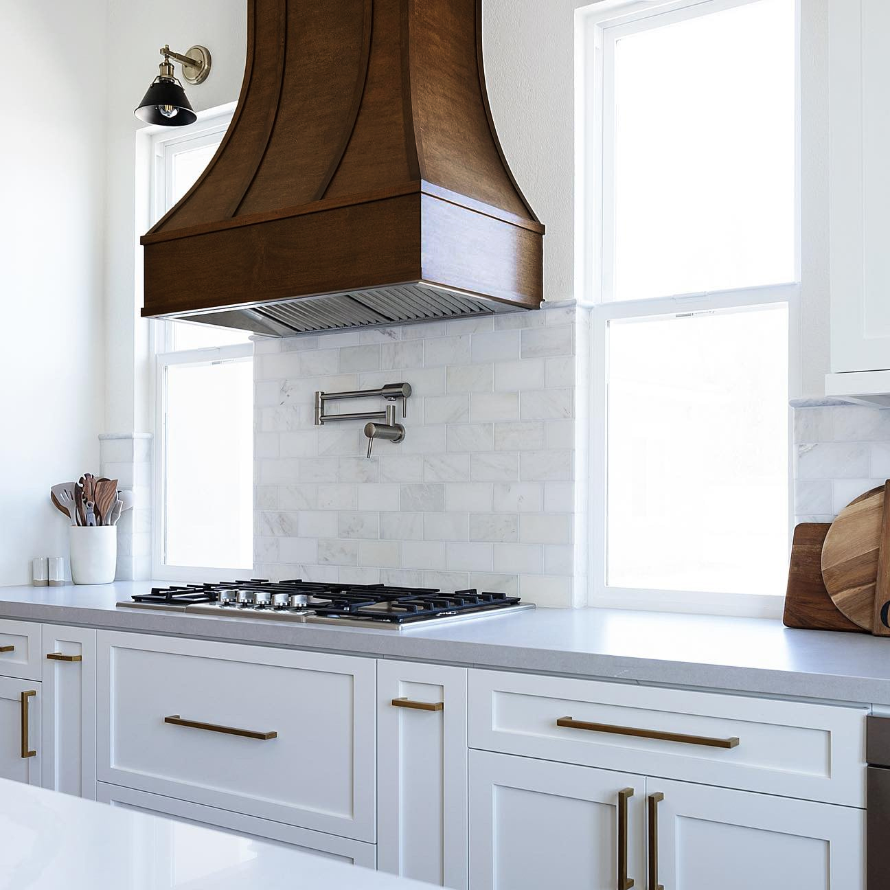 Curved wood range hood with wood strapping in warm brown stain against white shaker cabinets Curved wood range hood with wood strapping in warm brown stain against white shaker cabinets