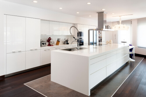 All-white one wall kitchen design with white high-gloss kitchen cabinets, minimal cabinet pulls and a large stainless steel chimney hood over the island All-white one wall kitchen design with white high-gloss kitchen cabinets, minimal cabinet pulls and a large stainless steel chimney hood over the island