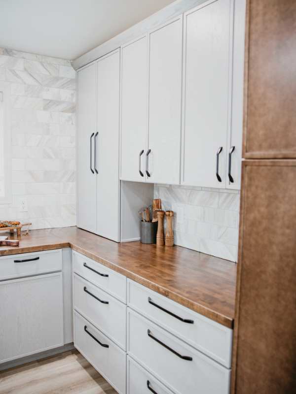 Tri-tone kitchen design with skinny shaker cabinets in light gray and medium brown with a black island and white stone countertops