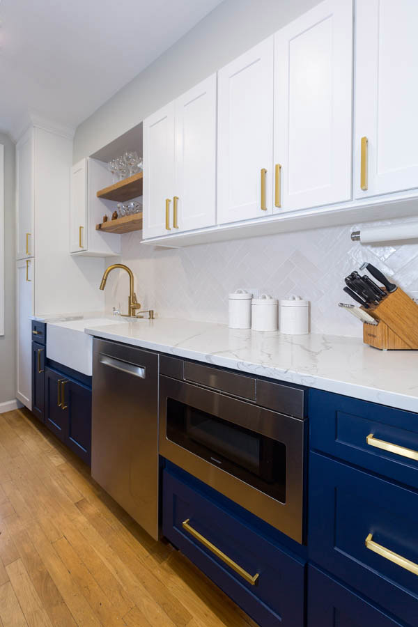 white kitchen with blue base cabinets, microwave cabinet next to stainless dishwasher and wood floating shelves above the sink white kitchen with blue base cabinets, microwave cabinet next to stainless dishwasher and wood floating shelves above the sink