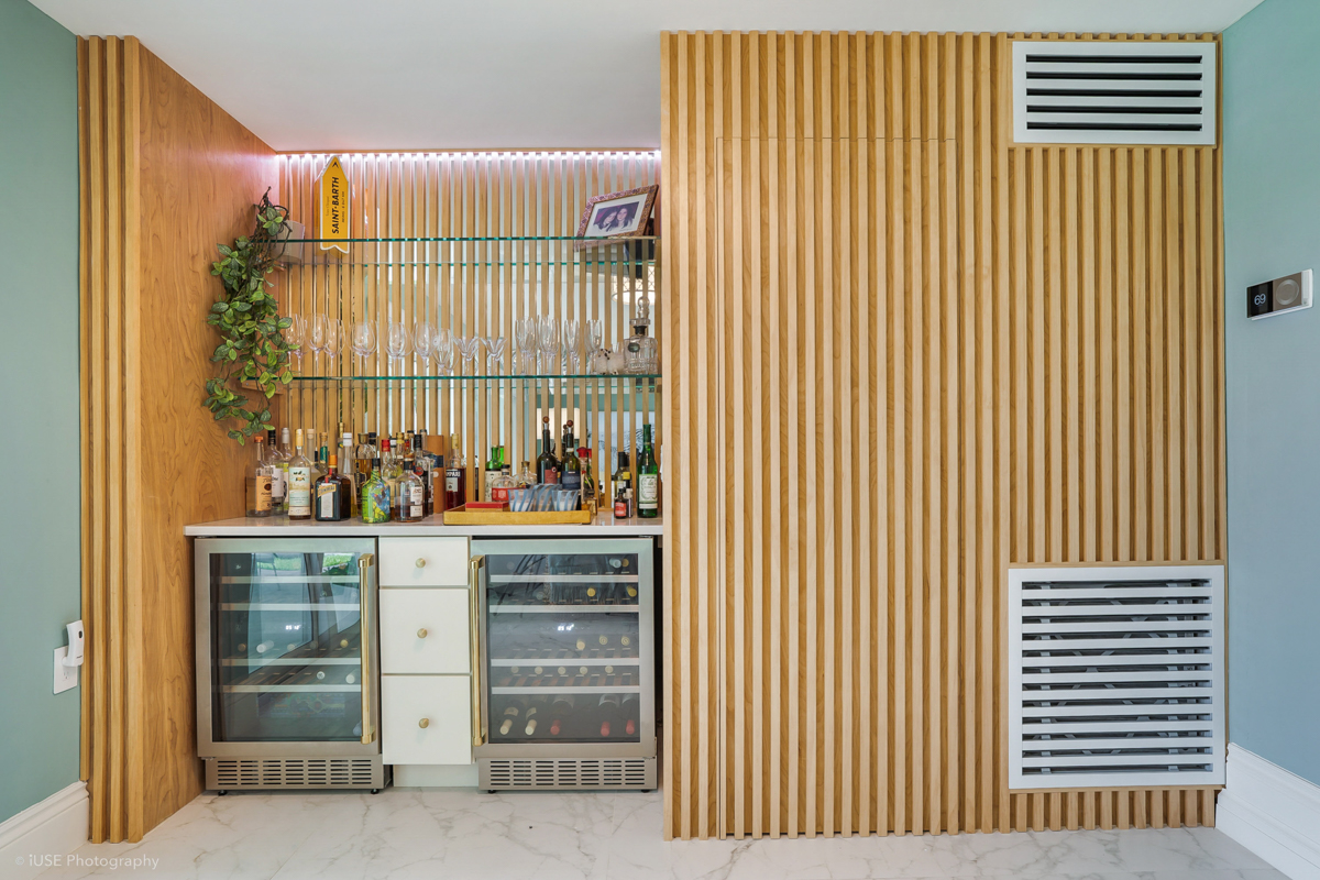 Built-in bar with two beverage coolers and a drawer base cabinet surrounded by vertical wood slat wall details Built-in bar with two beverage coolers and a drawer base cabinet surrounded by vertical wood slat wall details