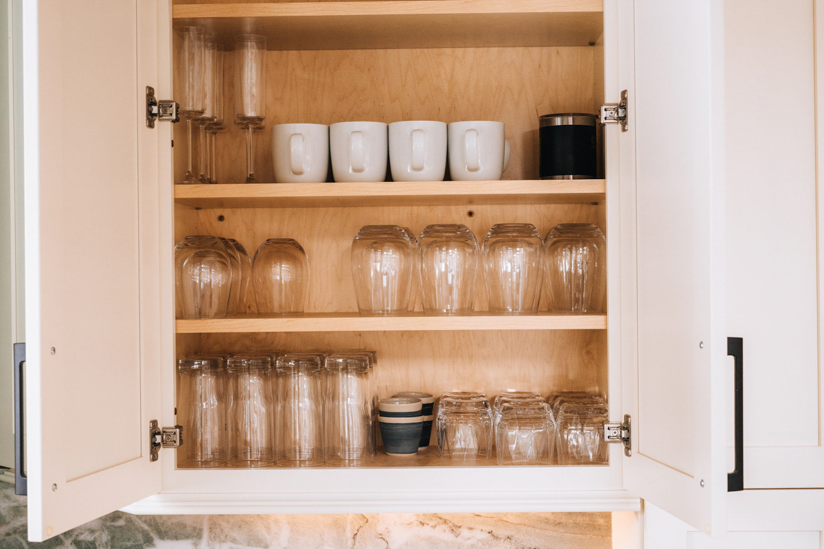 White shaker wall cabinet open displaying glassware and white coffee cups White shaker wall cabinet open displaying glassware and white coffee cups