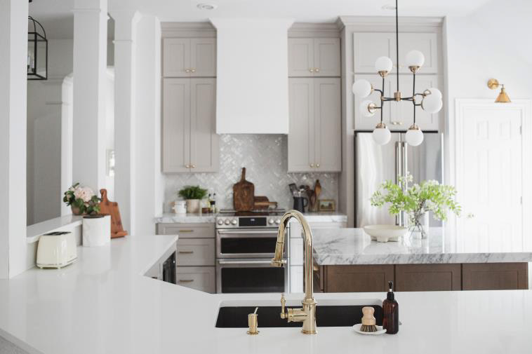Timeless Light Gray Kitchen Cabinets with Golden Knobs and Faucet. Light gray kitchen cabinets used with golden paint hardware. Gray and white textured countertops light up the look of the kitchen.