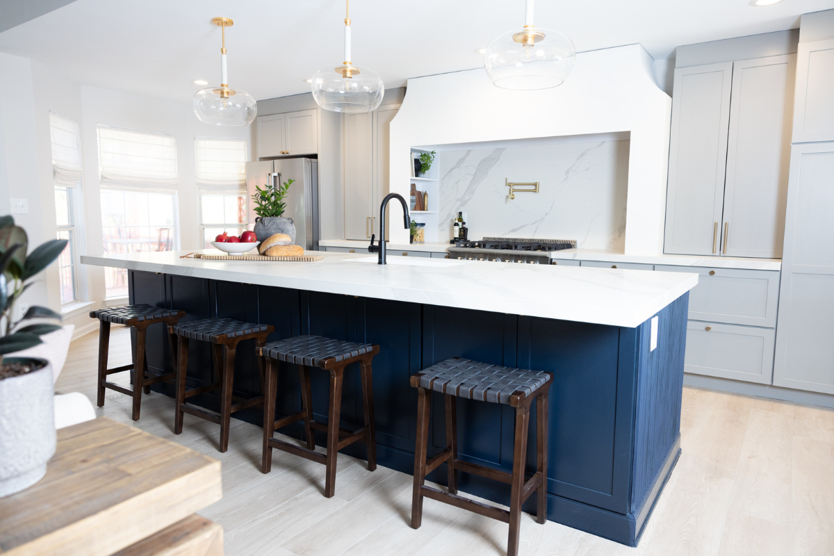 Large one-wall kitchen design with tall light gray shaker kitchen cabinets and gold cabinet hardware with a long dark blue kitchen island and white quartz countertops Large one-wall kitchen design with tall light gray shaker kitchen cabinets and gold cabinet hardware with a long dark blue kitchen island and white quartz countertops