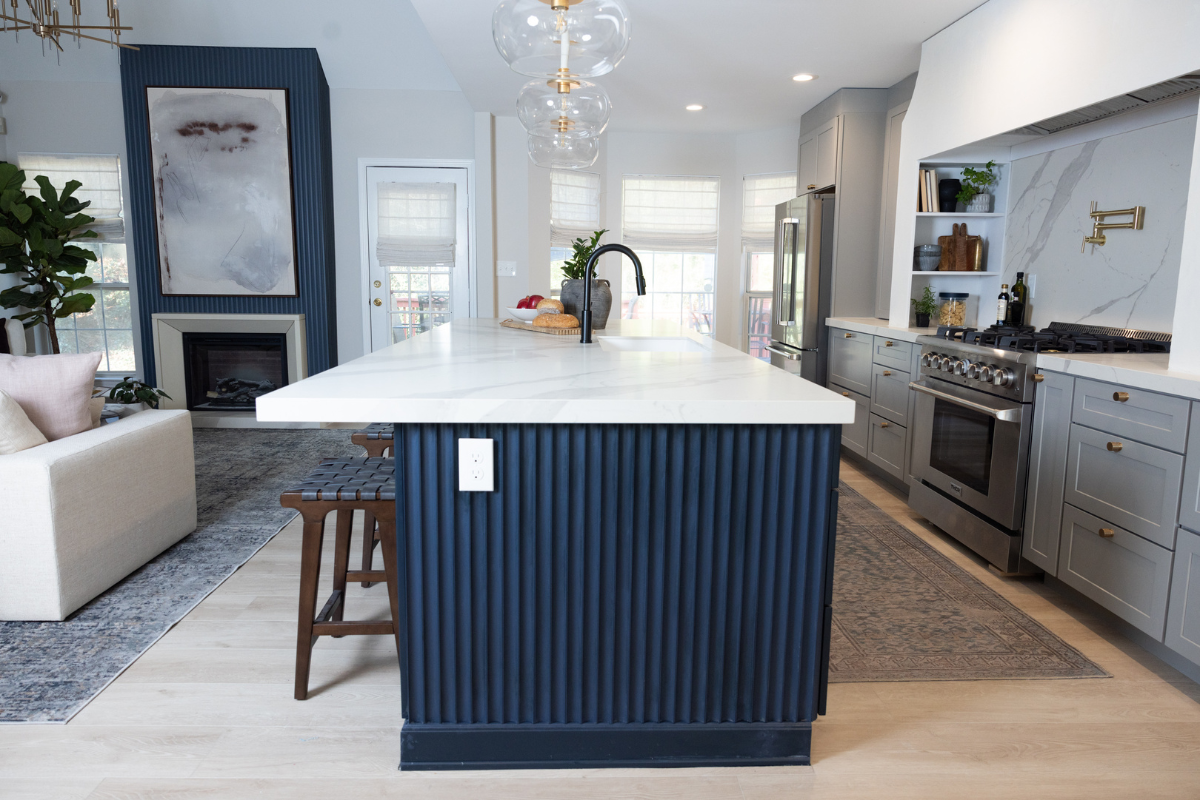 Large one-wall kitchen design with tall light gray shaker kitchen cabinets and gold cabinet hardware with a long dark blue kitchen island and white quartz countertops Large one-wall kitchen design with tall light gray shaker kitchen cabinets and gold cabinet hardware with a long dark blue kitchen island and white quartz countertops