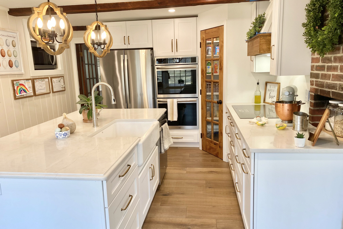 White shaker farmhouse kitchen with rustic wood beams, a large island, white quartz countertops and a large matching kitchen hood. White shaker farmhouse kitchen with rustic wood beams, a large island, white quartz countertops and a large matching kitchen hood.