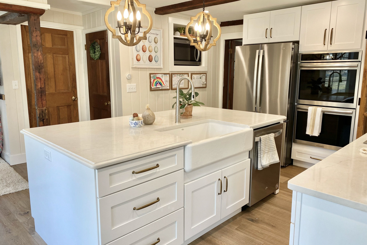White shaker farmhouse kitchen with rustic wood beams, a large island, white quartz countertops and a large matching kitchen hood. White shaker farmhouse kitchen with rustic wood beams, a large island, white quartz countertops and a large matching kitchen hood.