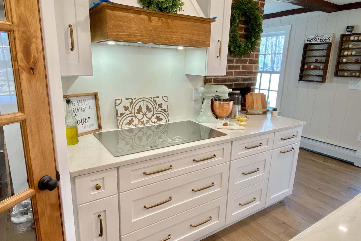 White shaker farmhouse kitchen with rustic wood beams, a large island, white quartz countertops and a large matching kitchen hood. White shaker farmhouse kitchen with rustic wood beams, a large island, white quartz countertops and a large matching kitchen hood.