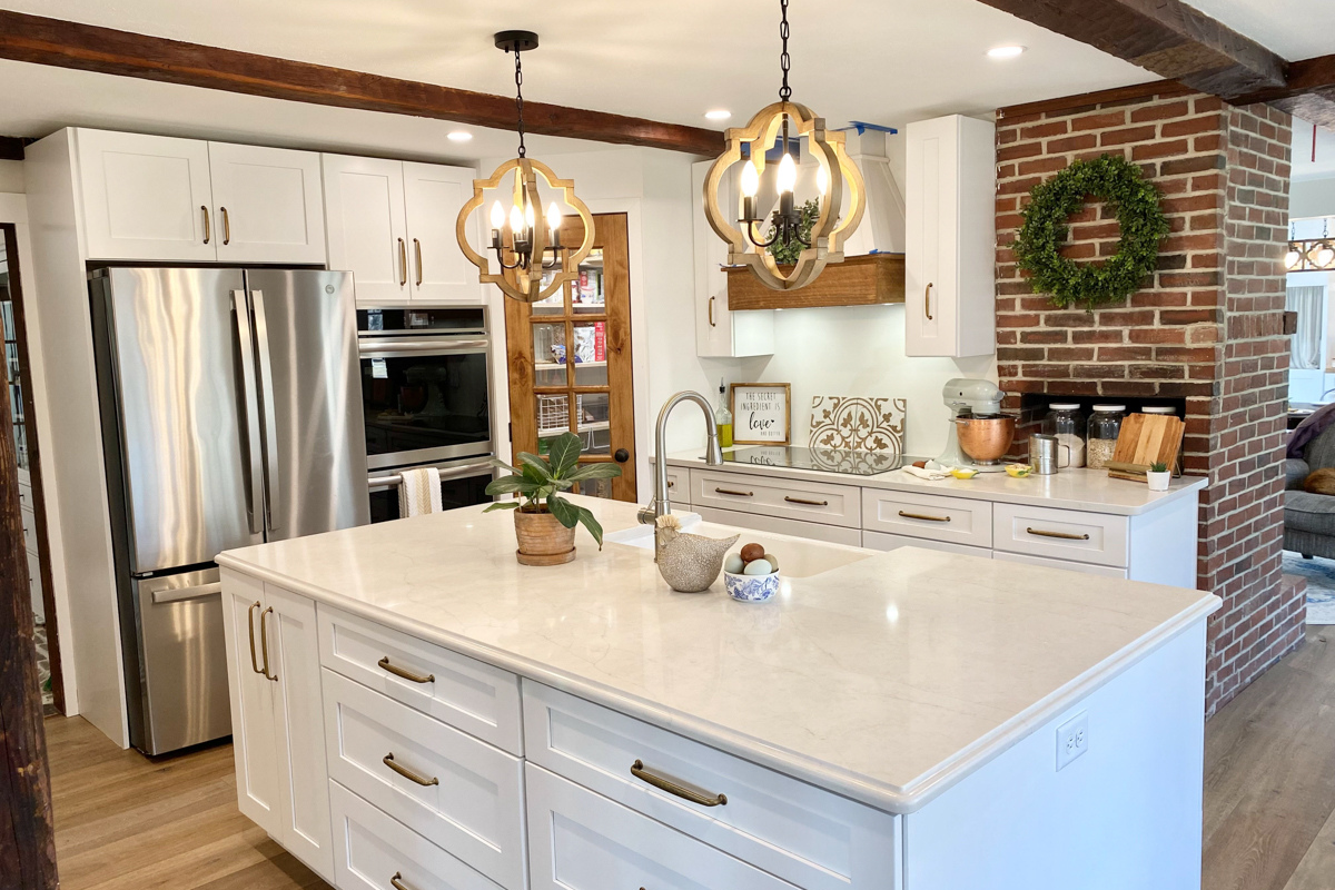 White shaker farmhouse kitchen with rustic wood beams, a large island, white quartz countertops and a large matching kitchen hood. White shaker farmhouse kitchen with rustic wood beams, a large island, white quartz countertops and a large matching kitchen hood.