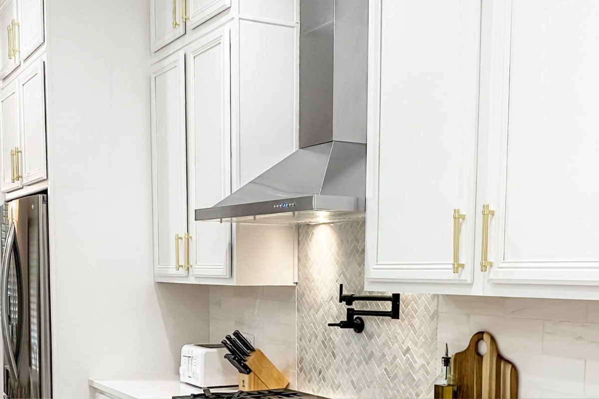 Wall-mount angled stainless steel range hood between white decorative cabinets Wall-mount angled stainless steel range hood between white decorative cabinets
