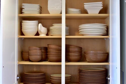 White wall cabinet with organized white and brown plates and bowls inside White kitchen shelving and storage with dishes inside