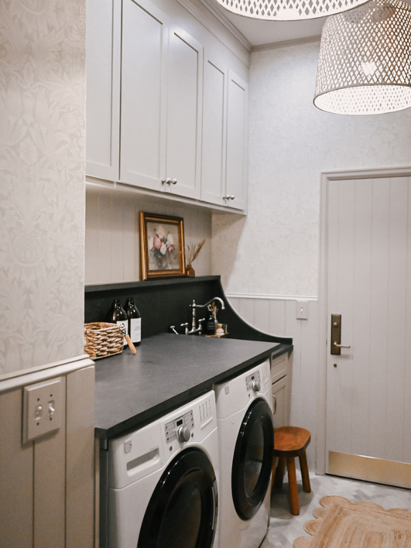 Left side of the laundry room with light taupe shaker wall cabinets above matching shiplap and black quartz countertops over a washer/dryer and sink Left side of the laundry room with light taupe shaker wall cabinets above matching shiplap and black quartz countertops over a washer/dryer and sink