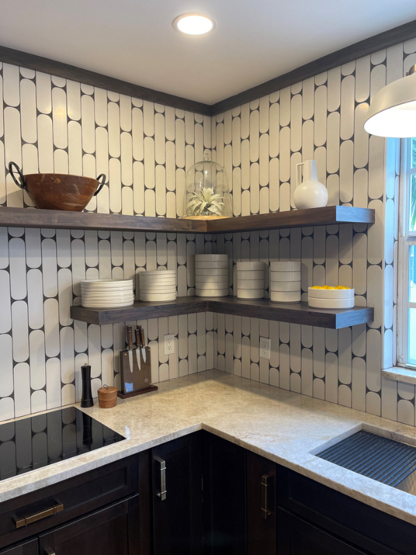Small and chic U-shaped kitchen in dark brown shaker cabinets with wood floating shelves, white funky tile backsplash, and light brown quartz countertop with waterfall edge detail Small and chic U-shaped kitchen in dark brown shaker cabinets with wood floating shelves, white funky tile backsplash, and light brown quartz countertop with waterfall edge detail