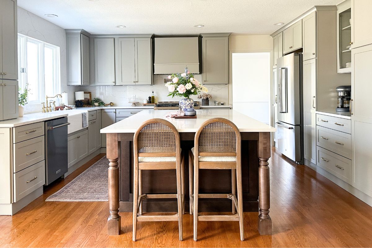 Light gray shaker kitchen with wood hood, white quartz countertops, and a large dark brown furniture-style island Light gray shaker kitchen with wood hood, white quartz countertops, and a large dark brown furniture-style island