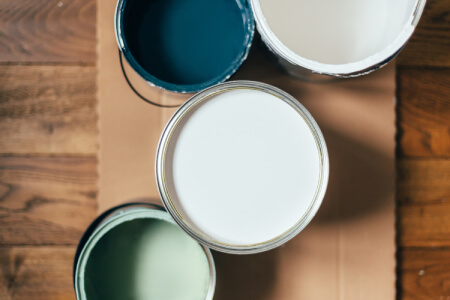 Four different paint cans with different shades of white, sage green and teal inside.
