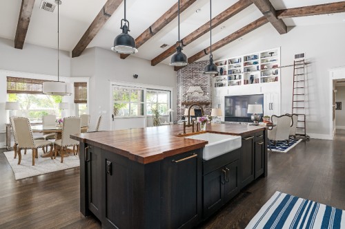 Large open kitchen and living room layout Large open kitchen and living room layout with black shaker island with butcher block countertops and a built-in white shaker entertainment center in the background with open cabinet storage above
