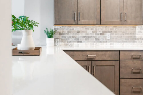 Medium-brown shaker kitchen cabinets with brushed nickel pulls Medium-brown shaker kitchen cabinets with brushed nickel pulls and white quartz countertops