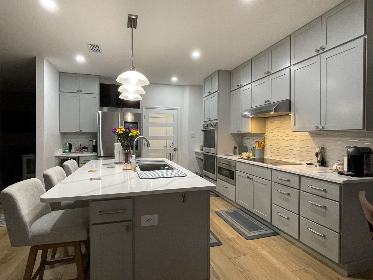 Light gray stacked shaker kitchen cabinets and island with white quartz countertops, brushed nickel cabinet hardware and modern pendant lighting Light gray stacked shaker kitchen cabinets and island with white quartz countertops, brushed nickel cabinet hardware and modern pendant lighting