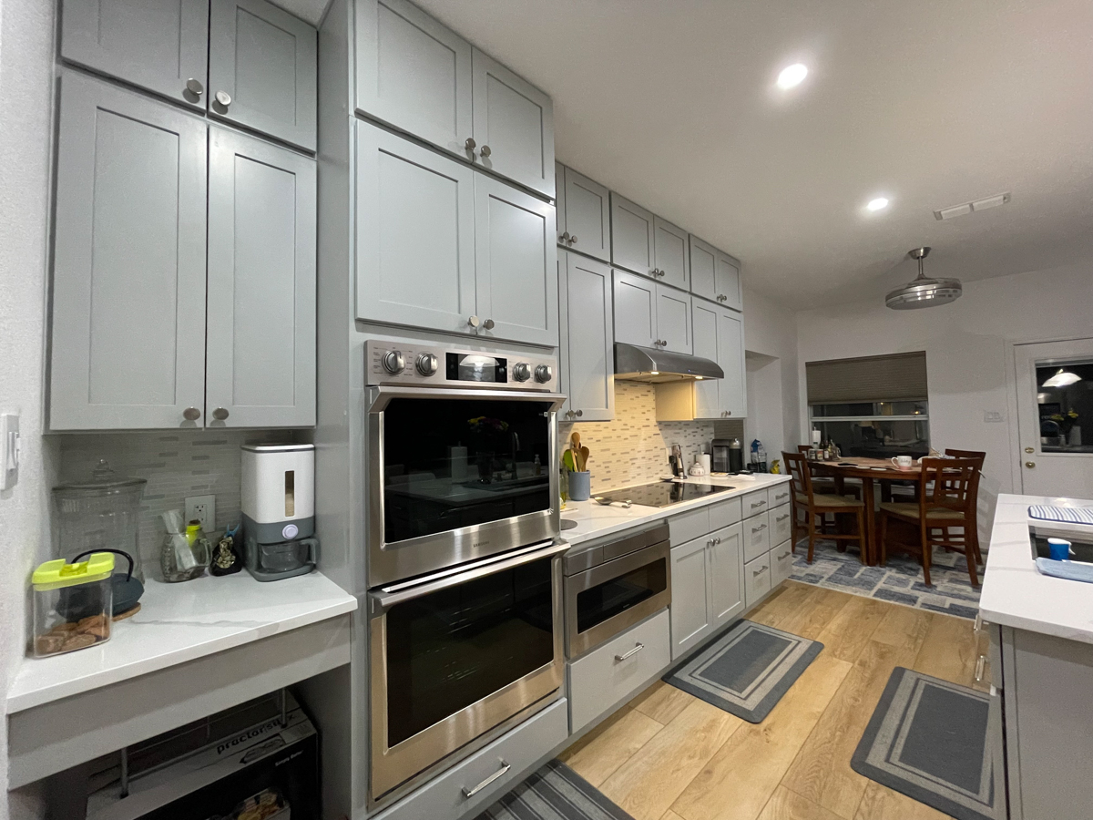 Light gray stacked shaker kitchen cabinets and island with white quartz countertops, brushed nickel cabinet hardware and modern pendant lighting Light gray stacked shaker kitchen cabinets and island with white quartz countertops, brushed nickel cabinet hardware and modern pendant lighting