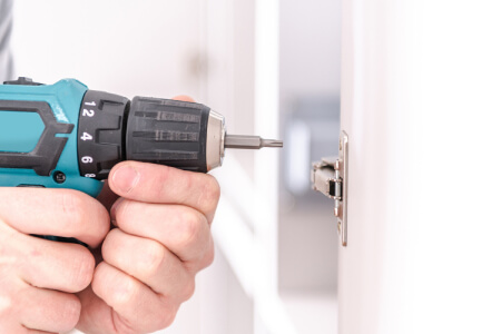 Power drill being held up to cabinet door hinge