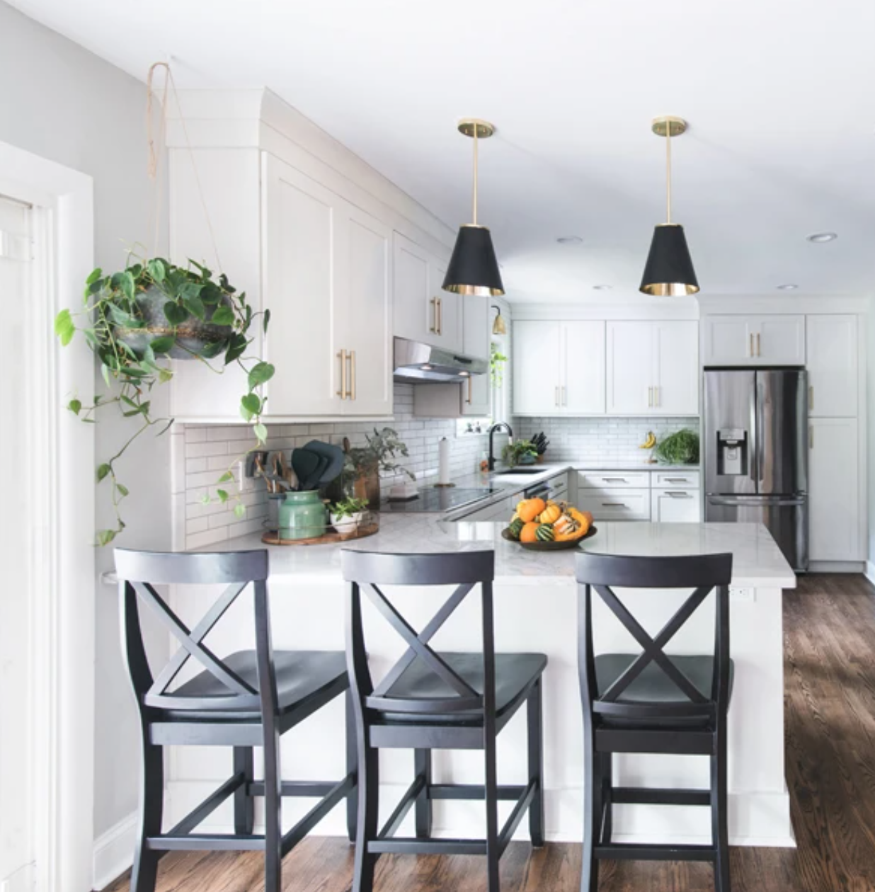 Long L-shaped white shaker-style kitchen and peninsula with gold hardware and black accents Long L-shaped white shaker-style kitchen and peninsula with gold hardware and black accents