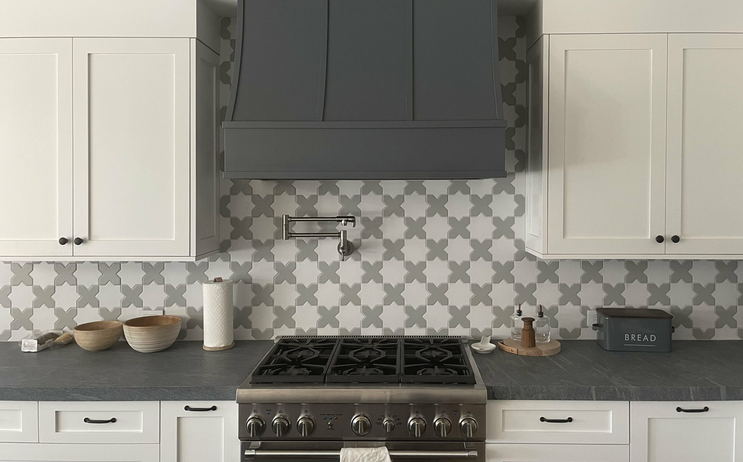 Sloped wood range hood with strapping in dark gray against taupe shaker cabinets Sloped wood range hood with strapping in dark gray against taupe shaker cabinets