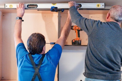 Two contractors installing wall cabinets and double-checking accuracy with a large level across the top Two contractors installing wall cabinets and double-checking accuracy with a large level across the top