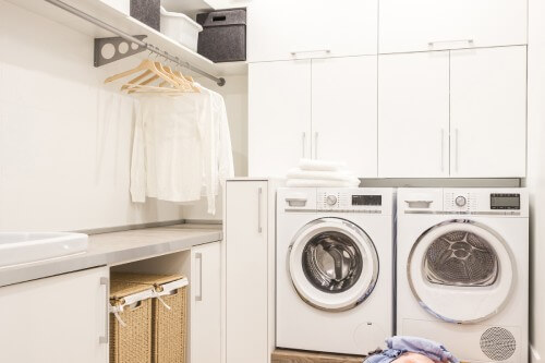White slab laundry room design with hanging rod above countertops White slab laundry room design with hanging rod above countertops