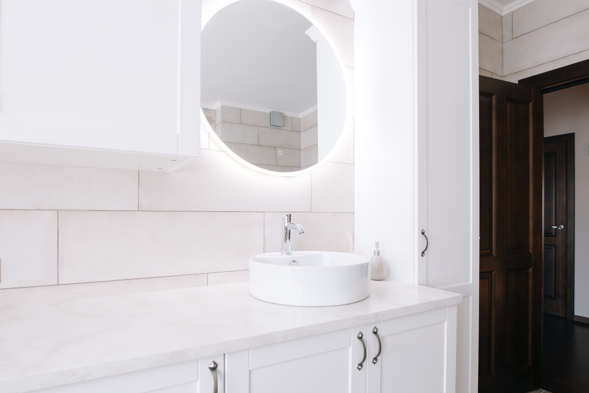 White shaker bathroom vanity cabinet with satin nickel hardware and circular mirror lit from behind White shaker bathroom vanity cabinet with satin nickel hardware and circular mirror lit from behind