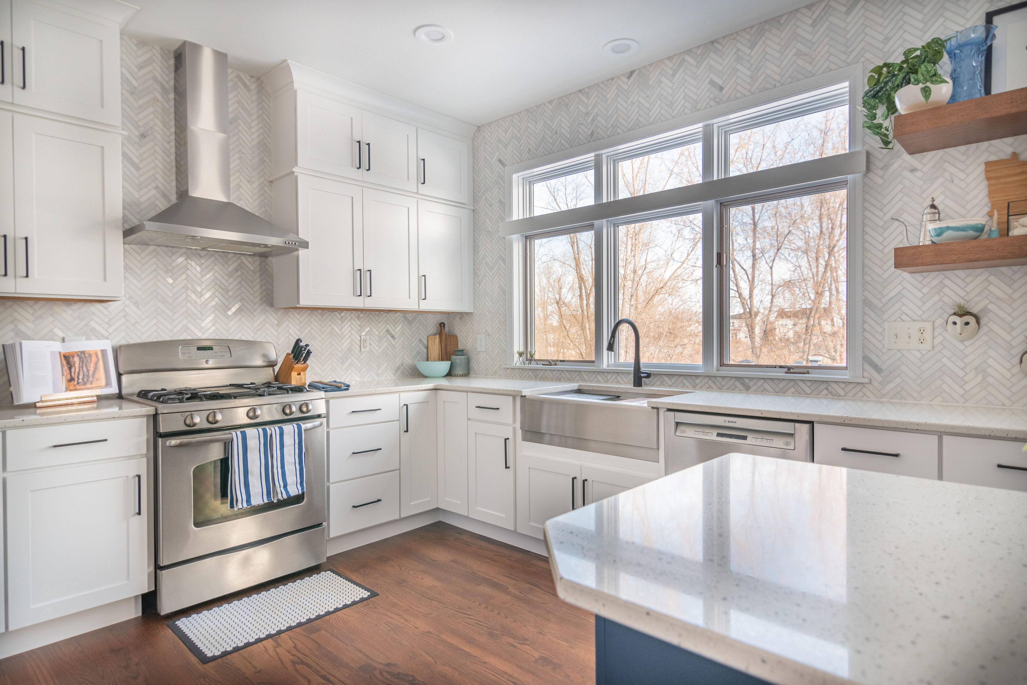 CliqStudios project: Stacked white shaker kitchen cabinets with a large window over the sink, marble herringbone tile, and warm wood floating shelves CliqStudios project: Stacked white shaker kitchen cabinets with a large window over the sink, marble herringbone tile, and warm wood floating shelves