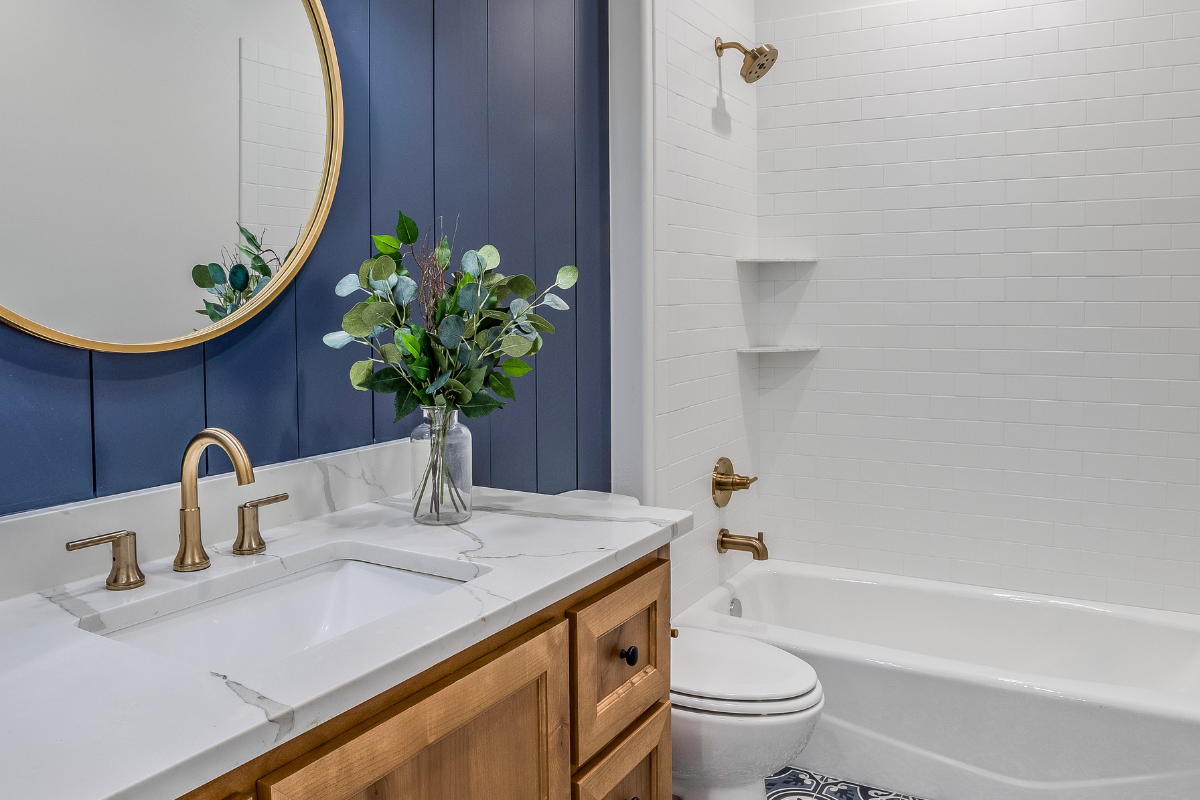 Light wood shaker vanity cabinet with marble countertop next to bright blue wall paneling and a matching round wood mirror Light wood shaker vanity cabinet with marble countertop next to bright blue wall paneling and a matching round wood mirror