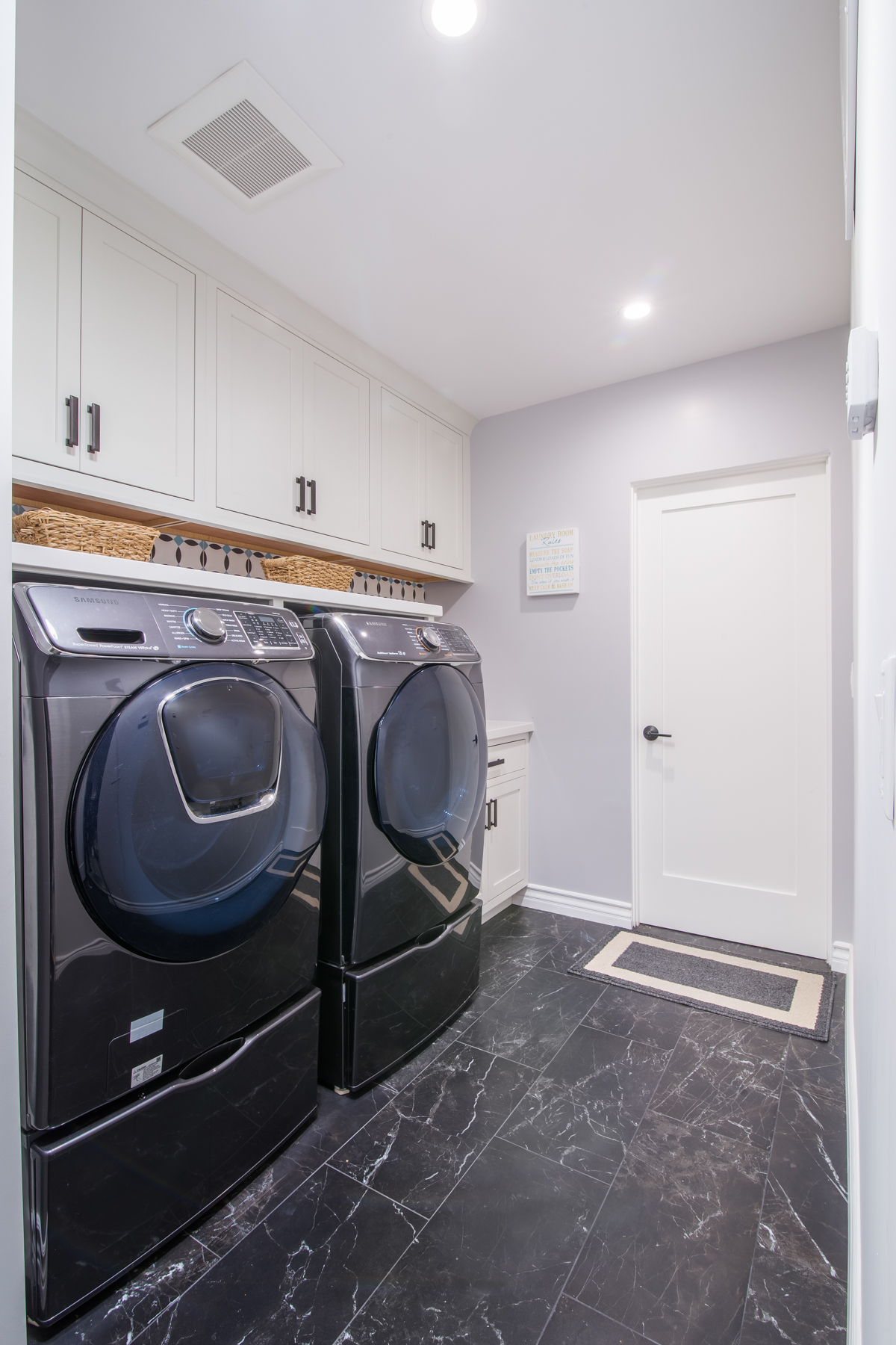 Inset shaker laundry room cabinets above a new frontload washer and dryer set. This image is of frontload washer and dryer set placed under the white laundry room cabinets.