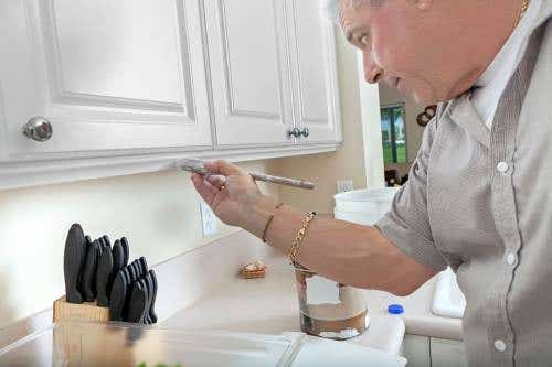Man hand-painting white raised panel wall cabinets with chrome knobs Man hand-painting white raised panel wall cabinets with chrome knobs