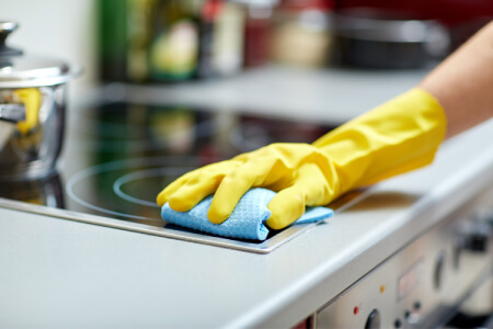 Person cleaning a glass cooktop with yellow gloves on