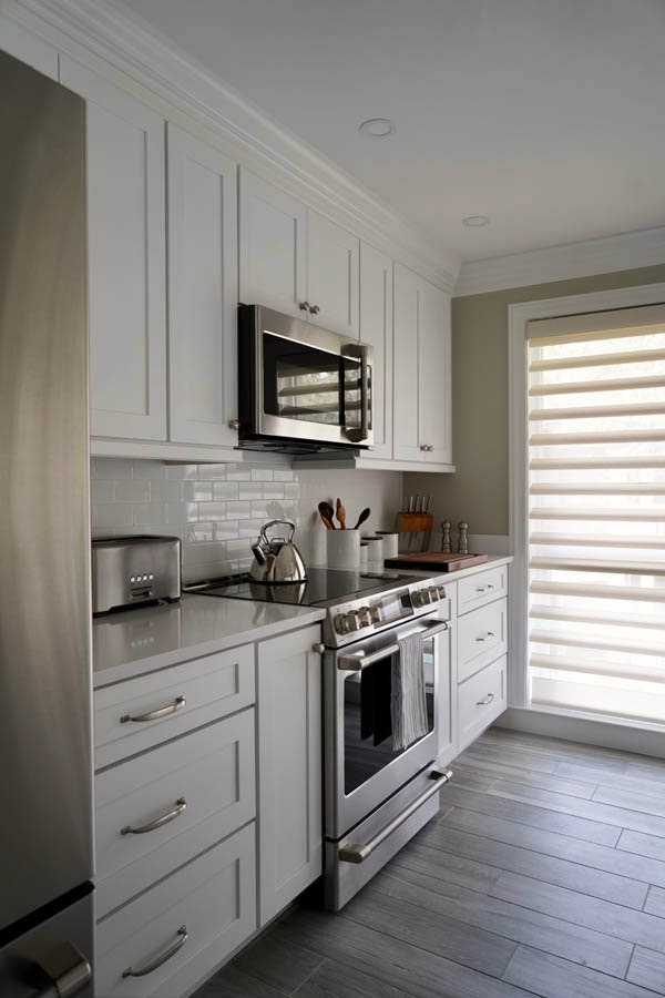 Kitchen wall with white cabinets, countertops and backsplash, with stainless oven and microwave Kitchen wall with white cabinets, countertops and backsplash, with stainless oven and microwave