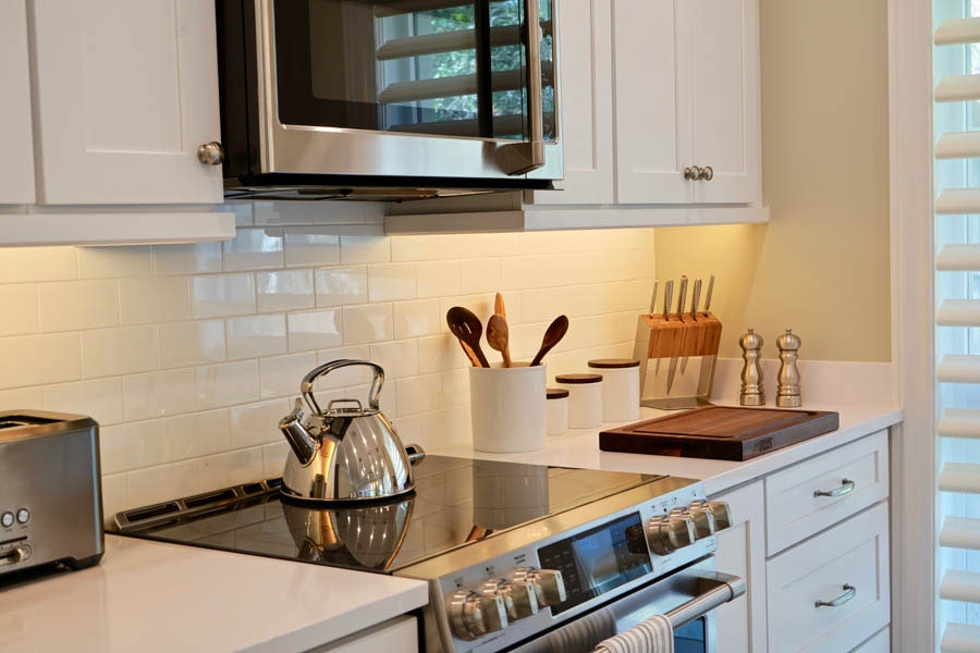 Stainless steel stove and microwave surrounded by white shaker cabinets, subway tile backsplash and white countertops Stainless steel stove and microwave surrounded by white shaker cabinets, subway tile backsplash and white countertops