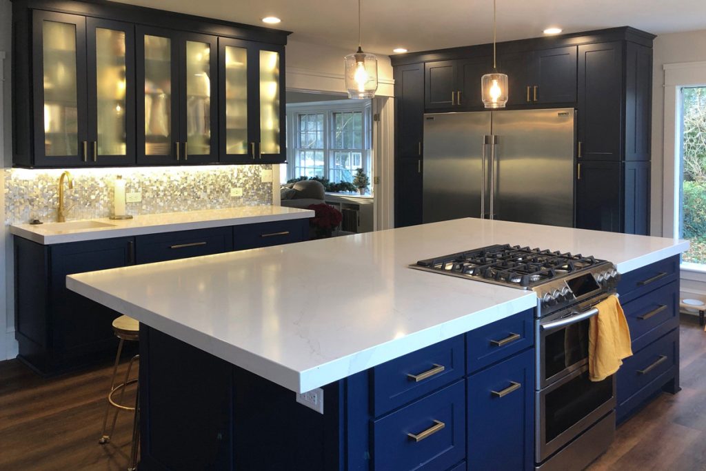 Large island with blue cabinets and white countertop facing pantry cabinets and second sink Large island with blue cabinets and white countertop facing pantry cabinets and second sink