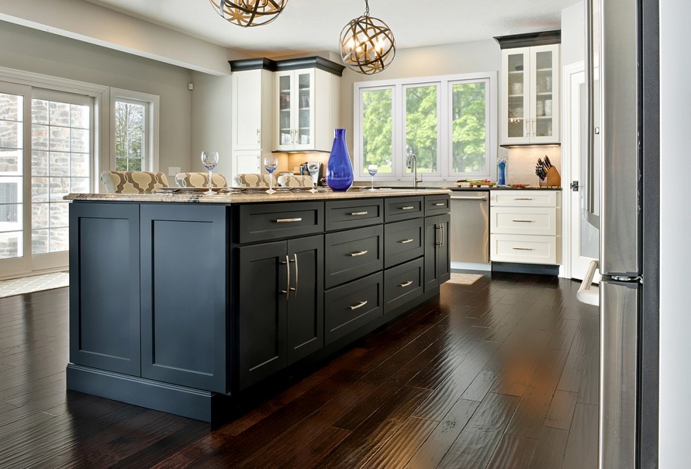 Open kitchen design in modern transitional style has large black island cabinets, black crown molding on white Shaker perimeter cabinets, and distressed hardwood flooring. Open kitchen design in modern transitional style has large black island cabinets, black crown molding on white Shaker perimeter cabinets, and distressed hardwood flooring.