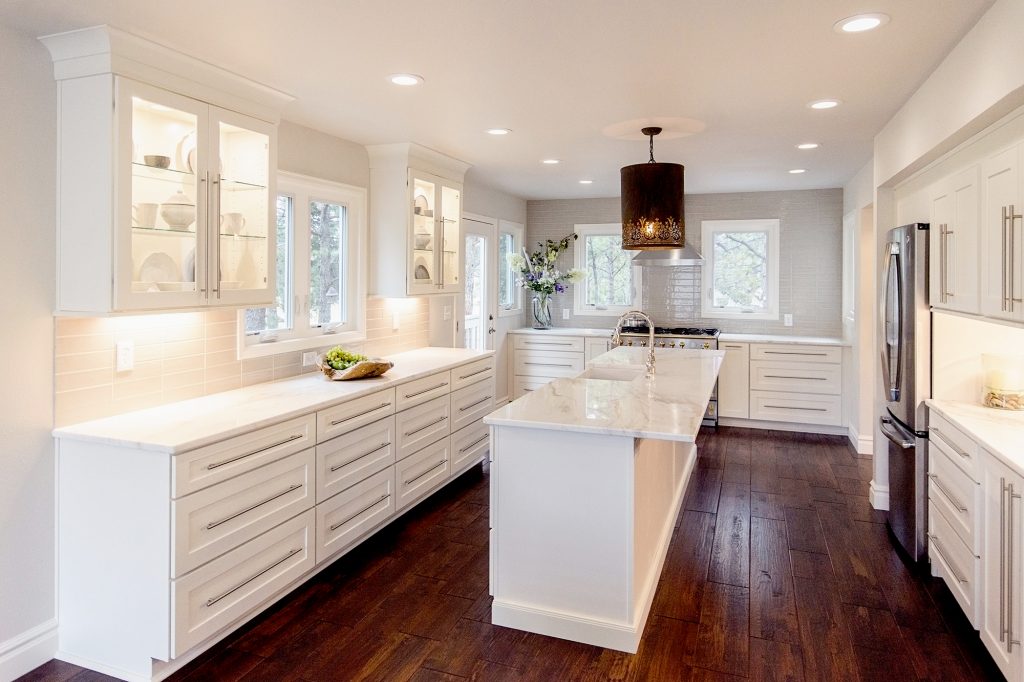 White shaker U-shaped kitchen design with long island in the center, glass wall cabinets, brushed nickel bar pulls, and white stone countertops White shaker U-shaped kitchen design with long island in the center, glass wall cabinets, brushed nickel bar pulls, and white stone countertops