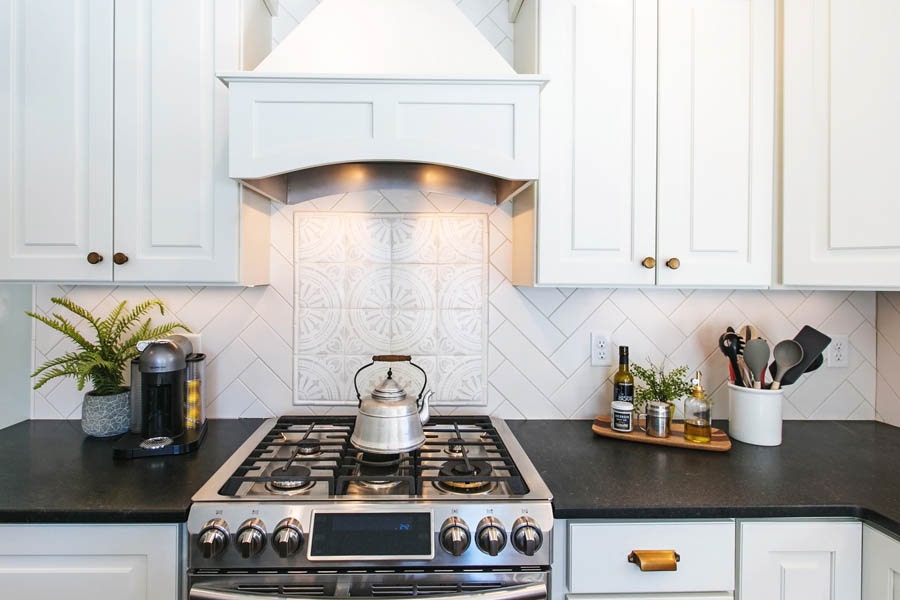 A kitchen stove top and wooden range hood with a white subway tile backsplash and a A kitchen stove top and wooden range hood with a white subway tile backsplash and a