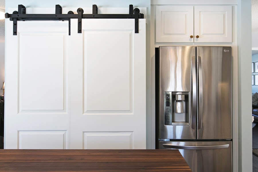 A white sliding farm door next to a stainless steel fridge. A white sliding farm door next to a stainless steel fridge.