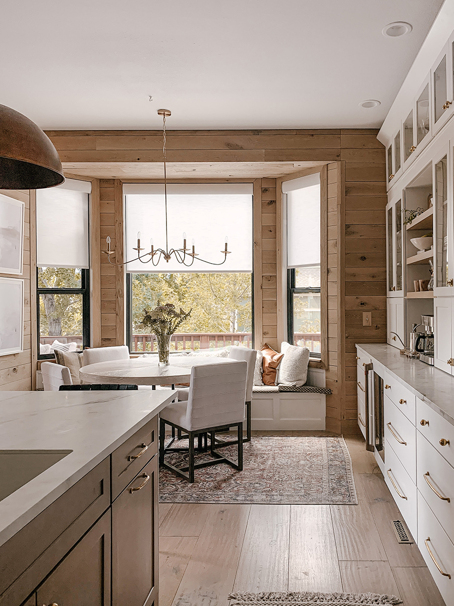 CliqStudios project: Light wood paneled breakfast nook with large window tucked in next to medium brown stained island and white shaker buffet kitchen cabinets CliqStudios project: Light wood paneled breakfast nook with large window tucked in next to medium brown stained island and white shaker buffet kitchen cabinets