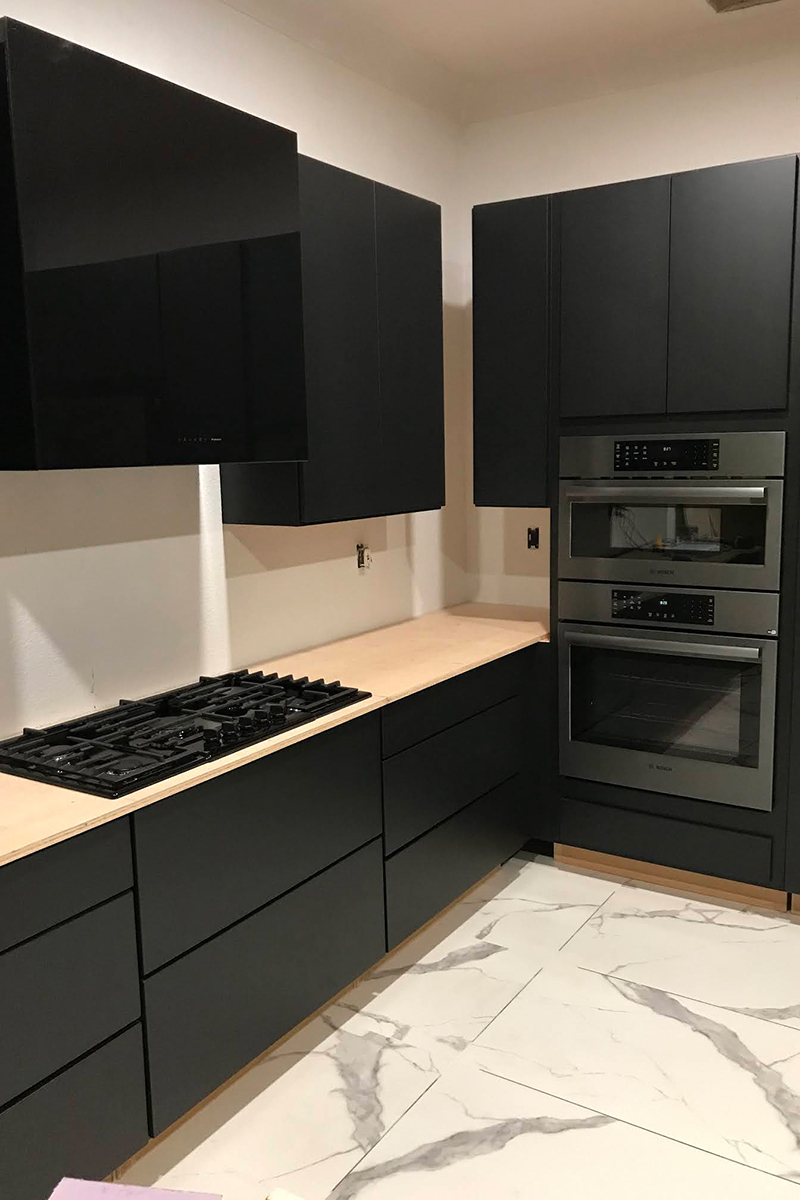 Black painted kitchen cabinets in slab door, dark appliances, and white marble tiled floors Black painted kitchen cabinets in slab door, dark appliances, and white marble tiled floors