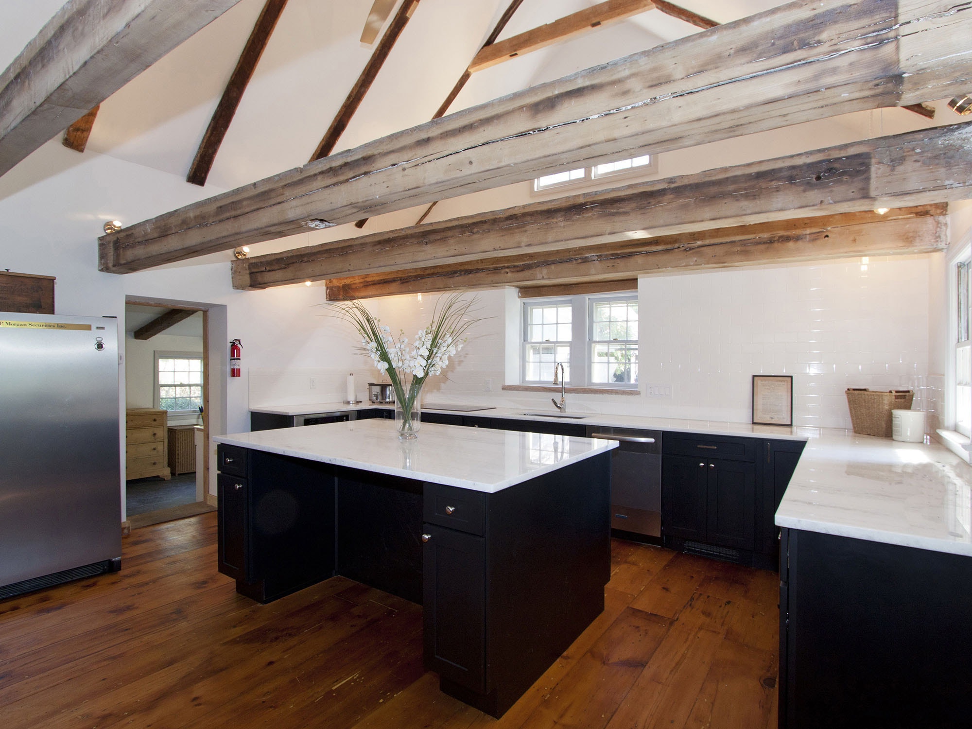 rustic luxe kitchen with broad exposed beams, wide plank floor with scraped paint, black shaker cabinets and white marble countertops and subway tile backsplash