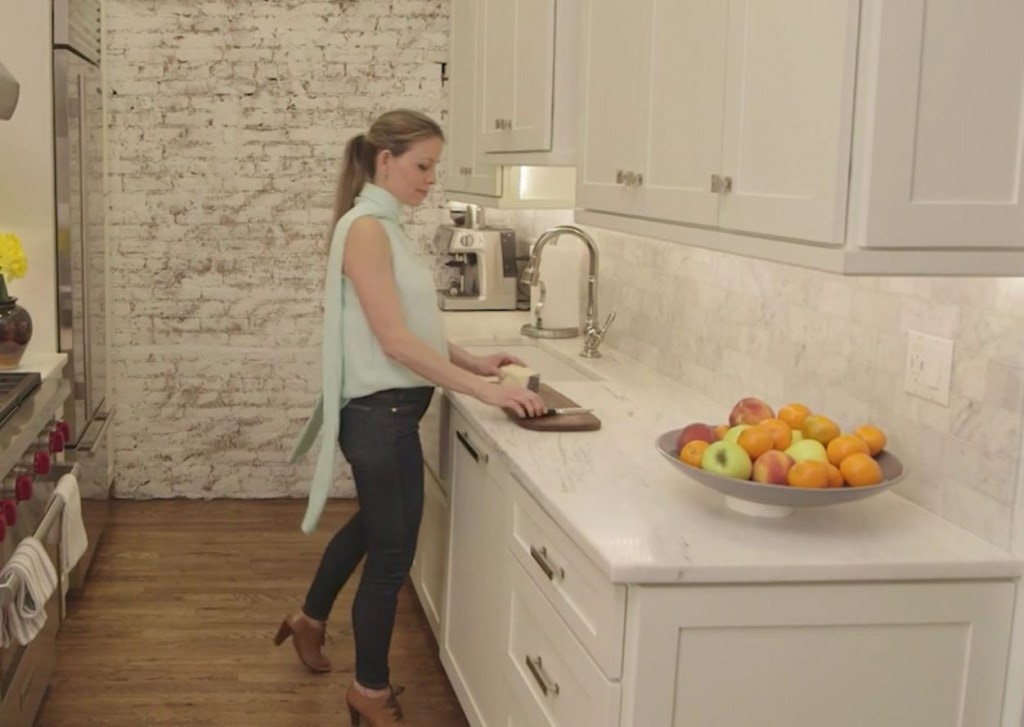 woman in kitchen with white cabinets, white marble countertops and paneled dishwasher cuts fruit woman in kitchen with white cabinets, white marble countertops and paneled dishwasher cuts fruit