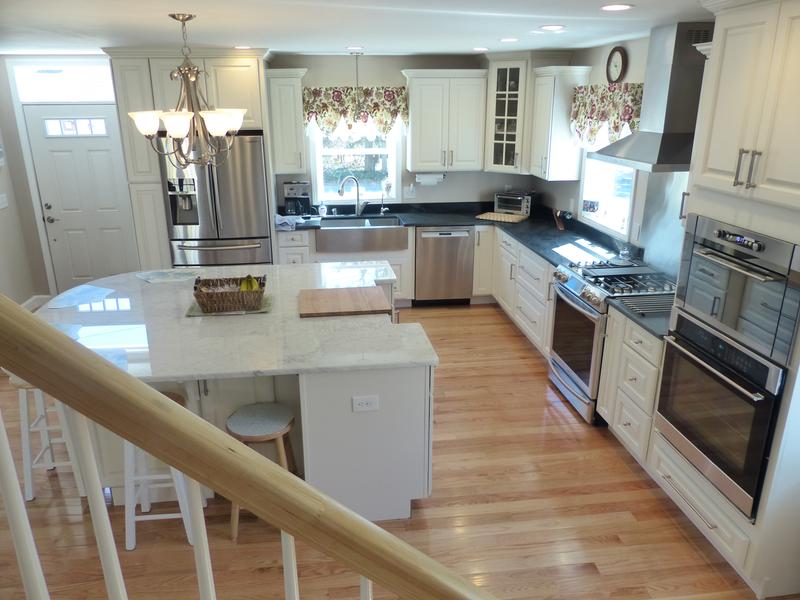 kitchen viewed from staircase has wide plank white oak flooring, painted white traditional cabinets, built-in ovens, glass mullion door cabinet, black granite countertops and large island with white granite counter. kitchen viewed from staircase has wide plank white oak flooring, painted white traditional cabinets, built-in ovens, glass mullion door cabinet, black granite countertops and large island with white granite counter.