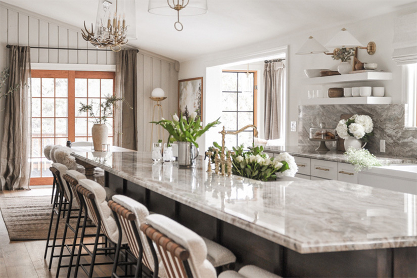 Newport Lily & Chai kitchen cabinets White shaker kitchen base cabinets and white floating shelves with a dark brown stained island and cream and brown granite countertops.