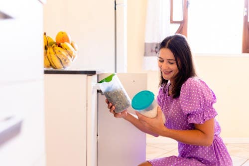 Smiling woman in a purple dress organizing dry goods in her kitchen Smiling woman organizing her kitchen